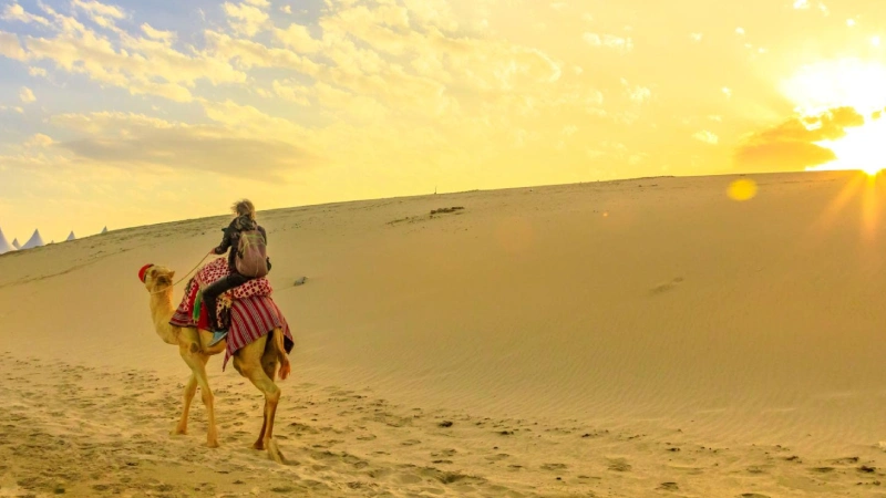 Dubai desert safari camel riding at sunset tourists on camel train across Arabian sand dunes | roamvisa.com