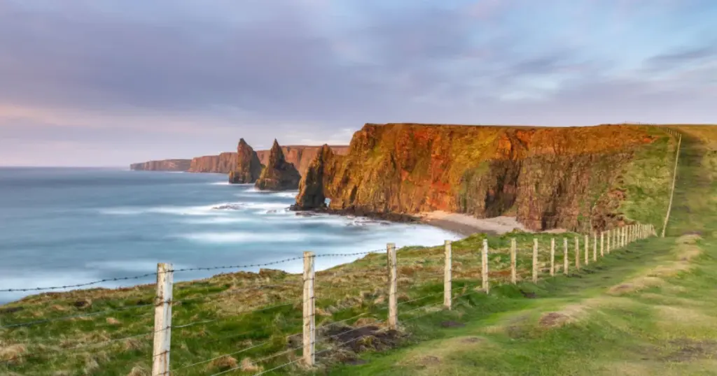 North Coast 500 Scotland route guide showing dramatic coastal clifftop road with turquoise bay and Duncansby sea stacks