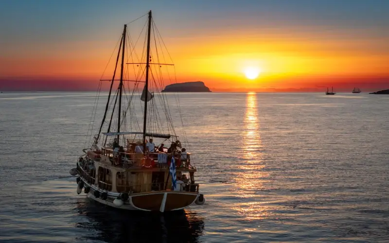 Catamaran sailing through the Santorini caldera during a colorful sunset cruise
