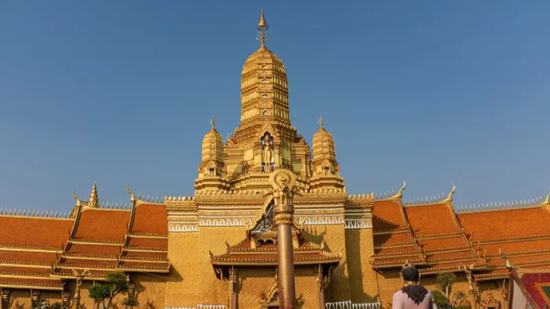 Golden Buddhist temple in Bangkok, Thailand, at sunset with tourists visiting