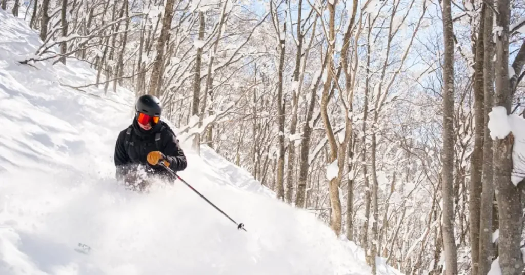Skier carving through fresh powder snow with the Northern Alps in the background Ski Holidays in Hakuba, Japan