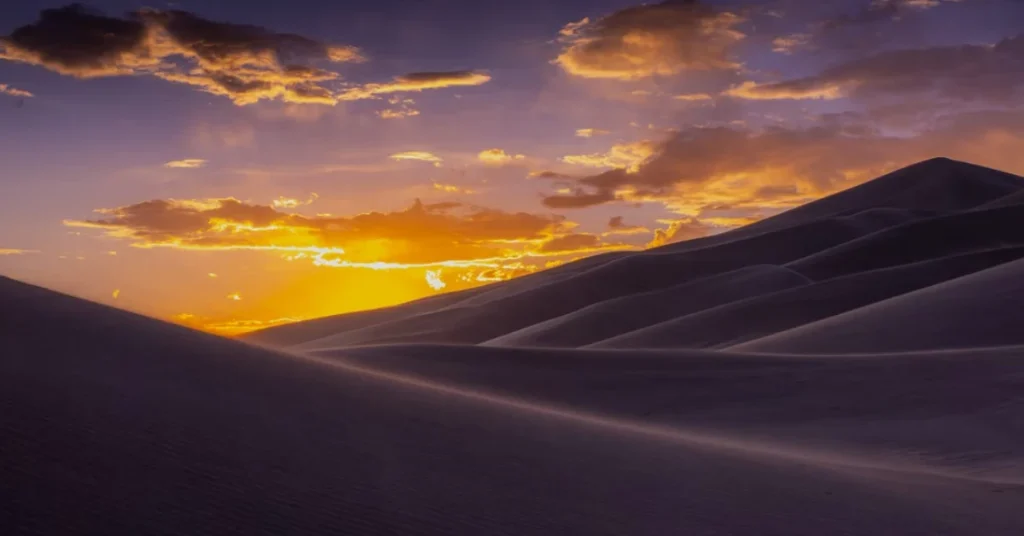 Tall sand dunes glowing at sunset with mountains in the background in Colorado